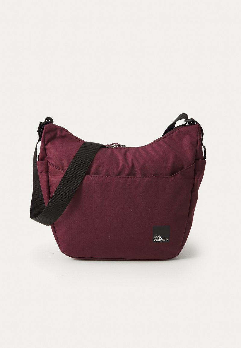 Burgundy fabric shoulder bag with a zippered closure, adjustable black strap, and logo patch. Soft, slightly padded material with a sleek design.