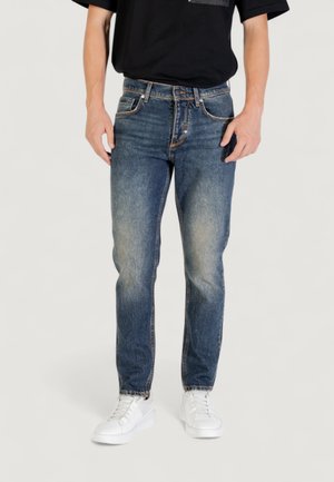 Jeans de mezclilla azul con corte recto, cintura media y un ligero desvanecimiento. Combinados con zapatillas blancas y una camiseta negra de manga corta.
