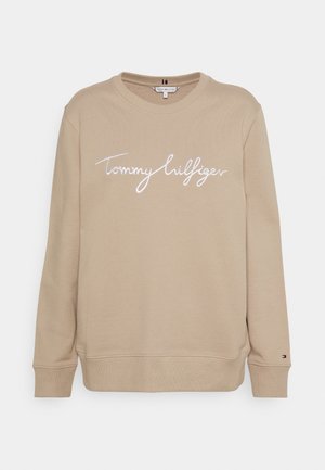 Beige langærmet sweatshirt med rund hals, hvide "Tommy Hilfiger"-bogstaver tværs over brystet og lille logo på venstre ærmekant.