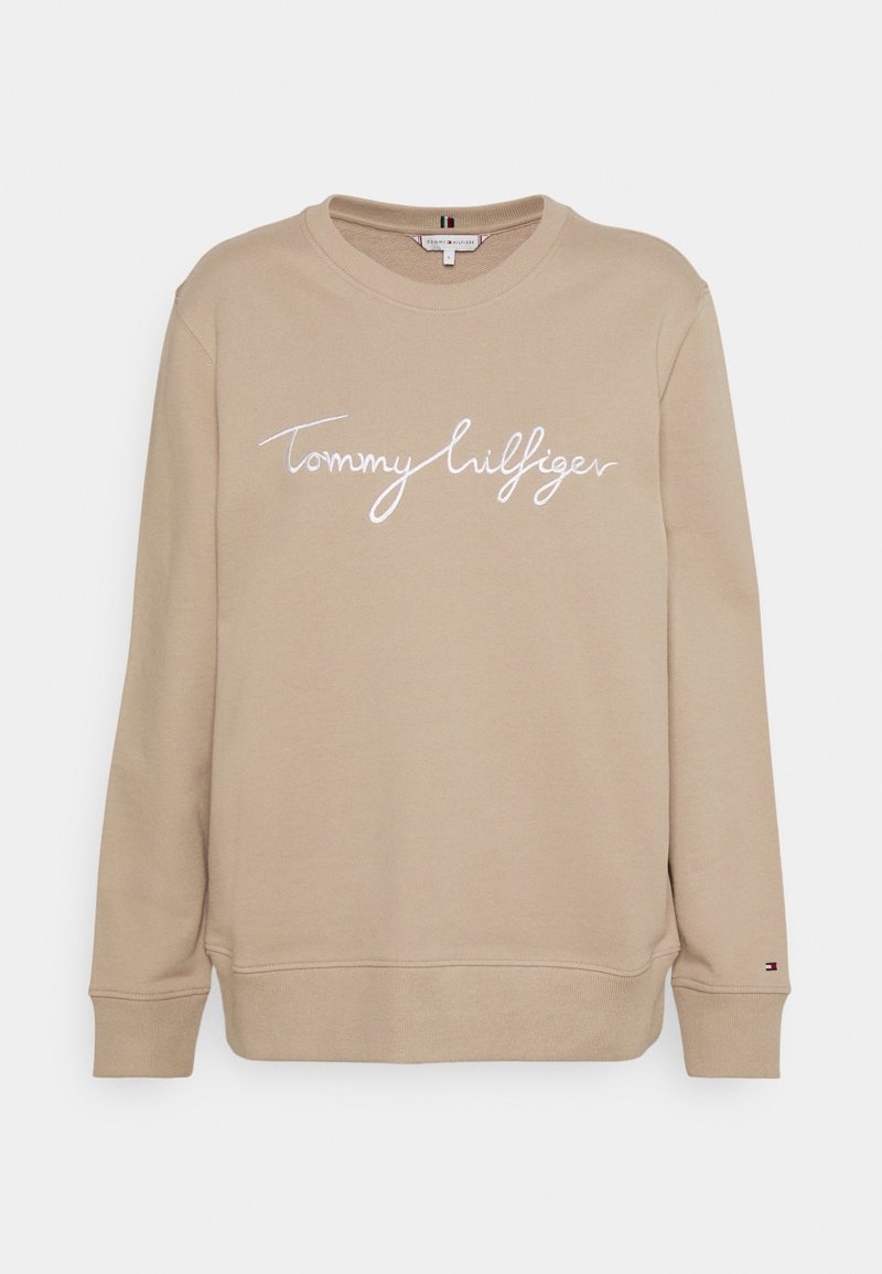 Sweat-shirt beige à manches longues avec col rond, portant l'inscription blanche "Tommy Hilfiger" sur la poitrine et un petit logo sur le poignet gauche.