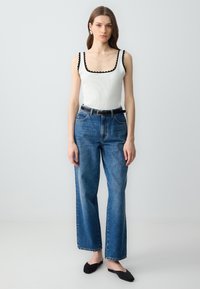 Top in cotone bianco con coste e bordo nero a scallop, abbinato a jeans blu a gamba dritta a vita alta e scarpe nere slip-on.