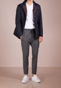 Granatowa pikowana kurtka z brązowym podbiciem, biała koszulka, szare zwężane spodnie i białe trampki. Teksturowana tkanina, zamek błyskawiczny oraz zapięcia na guziki.