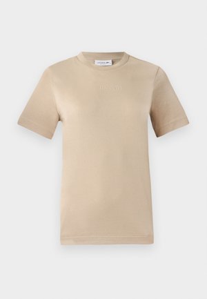 T-shirt de algodão bege, mangas curtas, gola redonda, apresentando o logótipo "LACOSTE" em relevo no peito, textura suave e ajuste padrão.