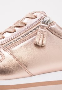Metalické růžovo-zlaté tenisky s texturovanou kůží, kulatou špičkou, šněrováním, bočním zipem a bílou podešví s hnědým pruhem.