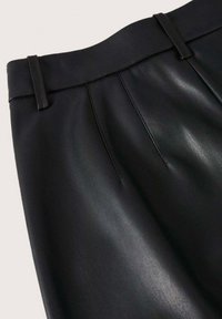 Gros plan sur un pantalon en similicuir noir montrant une taille haute, des passants de ceinture et des détails de coutures à l'avant.