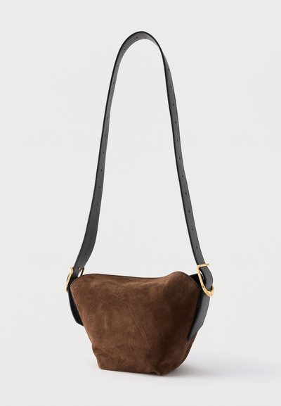Brun ruskindshåndtaske med en bred, justerbar sort læderrem med guldspænde-detaljer.