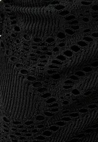Tissu noir présentant un motif en tricot ouvert texturé avec des trous irréguliers et des sections côtelées, créant un effet visuel superposé.