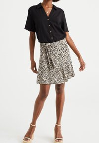 Zwarte kortefris shirt met knopen, gedragen met een gehaakt wikkelrok in beige, zwart en bruin, met een gerimpelde zoom en enkelband wedgeschoenen.