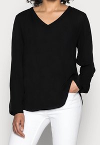 Zwarte lange mouwen V-hals blouse in lichtgewicht stof met een relaxte pasvorm, voorzien van zijsplitten en een zachte textuur. Gecombineerd met witte broek.