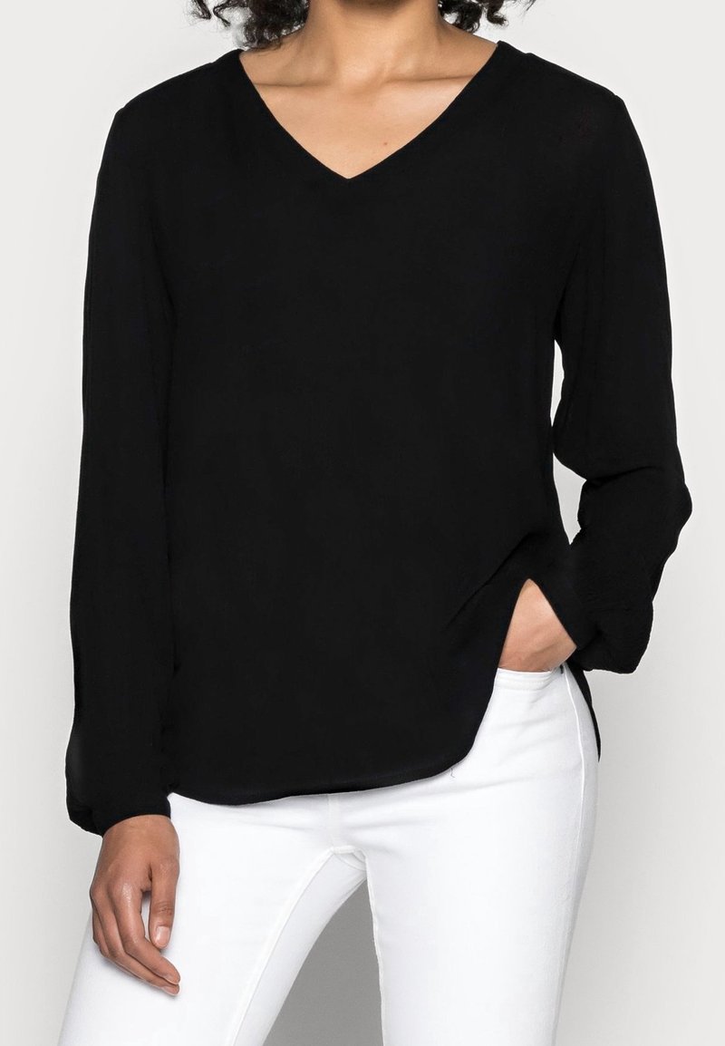 Zwarte lange mouwen V-hals blouse in lichtgewicht stof met een relaxte pasvorm, voorzien van zijsplitten en een zachte textuur. Gecombineerd met witte broek.