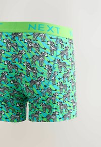 Zebra mintás élénk zöld boxer sort; kontrasztos neon derékkal rendelkezik, amelyen a "NEXT" logo és bonyolult varrási részletek találhatók.
