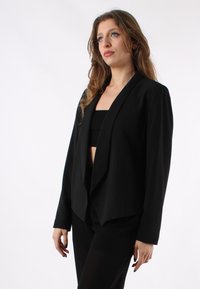 Blazer nero con colletto a punte, design con apertura frontale e tessuto liscio. Leggero con maniche lunghe, sartoriale per una silhouette aderente.