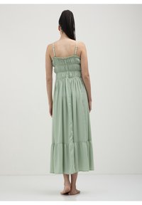 Robe longue vert clair à fines bretelles spaghetti, avec corsage froncé et ourlet à volants à étages. Tissu doux et fluide avec une texture lisse.