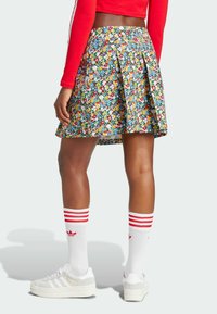 Falda plisada floral con un patrón colorido sobre un fondo oscuro, combinada con zapatillas blancas y calcetines a rayas rojas.