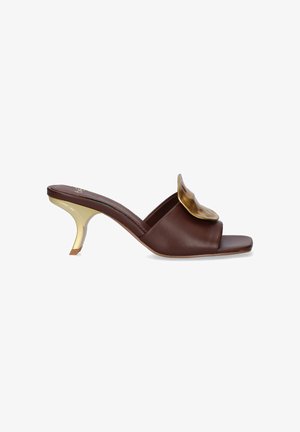 Mule marrón con punta abierta, tacón bajo dorado curvado y gran adorno dorado decorativo en la correa superior.