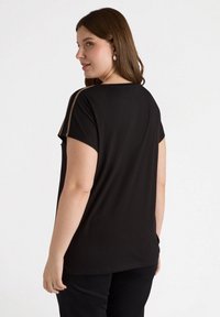 Camiseta negra de manga corta, con cuello redondo y franjas doradas en los hombros. Hecha de una tela ligera con un corte relajado.