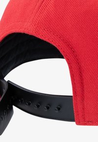 Rød kasket med blødt stof på ydersiden og en sort justerbar plastrem med flere huller til størrelse.