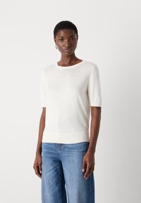 Pull court à manches courtes blanc en tissu léger, avec un col rond et un ourlet côtelé, associé à un jean large bleu clair.