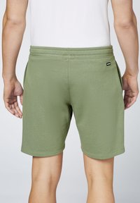 Grüne Baumwollshorts mit elastischem Bund, Seitentaschen und einem kleinen Markenlabel auf der Rückseite. Glatte Textur und taillierte Passform.