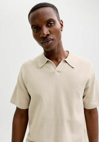 Polo beige à manches courtes avec un tricot texturé, un col en V et un col classique. Présente des détails de couture subtils.