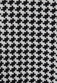 Tissu à motifs en noir et blanc présentant un motif pied-de-poule. La texture est tricotée, avec un motif répétitif de formes angulaires.