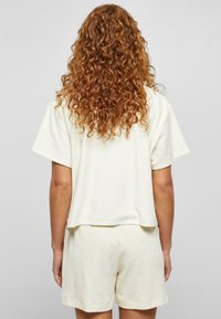 Kurzärmeliges, verkürztes T-Shirt und passende Shorts aus weichem, hellem Creme-Stoff. Auffällige strukturelle Oberfläche, lockere Passform und schlichtes Design.