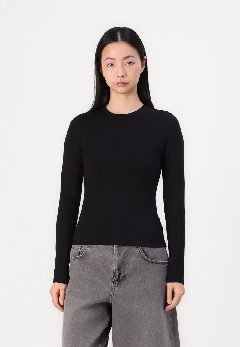 Schwarzes Longsleeve-Oberteil aus einem glatten, elastischen Stoff mit Rundhalsausschnitt. Kombiniert mit grauen, locker sitzenden Hosen, die einen lässigen Look kreieren.