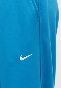 Φωτεινό γαλάζιο ύφασμα με μικρό λευκό λογότυπο Nike swoosh κεντημένο κοντά σε κάθετη ραφή και άκρη τσέπης.