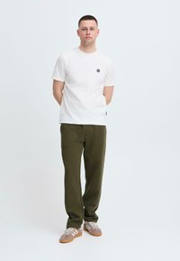 Hvit bomulls t-skjorte med en liten svart logo, paret med olivengrønne joggebukser og grå sneakers med hvite striper. Minimalistisk design.
