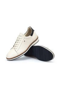 Zapatillas de cuero en color blanco roto con detalles en negro, que presentan un diseño de cordones, puntera redonda y una suela de goma texturizada negra.