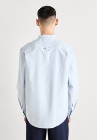 Ljusblå långärmad skjorta i mjukt tyg, med standardkrage, hel knappslå och svängd nederkant. Märket syns på baksidan.