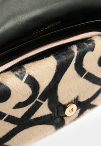 Sac en cuir noir avec un panneau beige doux à motifs abstraits noirs, quincaillerie dorée et doublure intérieure lisse.