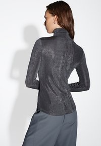 Top a collo alto e maniche lunghe in tessuto metallico nero, caratterizzato da una texture liscia e un design aderente con sottili righe verticali.