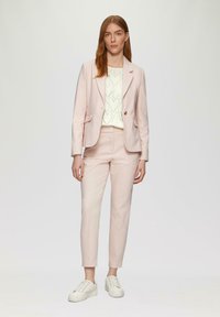 Blazer ajusté rose clair et pantalon assorti, associés à un pull blanc avec un motif en forme de cœur, complétés par des baskets blanches.