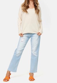 Beige långärmad topp i kombination med ljusblå slitna vida jeans och orange klacksandaler med fransdetaljer. Enkelt och avslappnat klädesplagg.