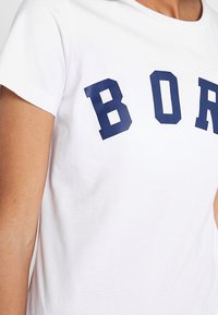 Biały bawełniany t-shirt z granatowymi blokowymi literami tworzącymi napis "BOR" na piersi. Krótkie rękawy i klasyczny okrągły dekolt.