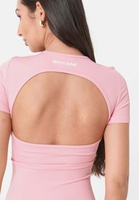 Lyserød ribbet top med rund halsudskæring og åben rygdesign. Stoffet har en glat tekstur, med branding øverst på ryggen.
