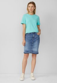 Un t-shirt bleu clair à manches courtes associé à une jupe crayon en denim bleu. La tenue comprend des baskets blanches et présente un design classique.
