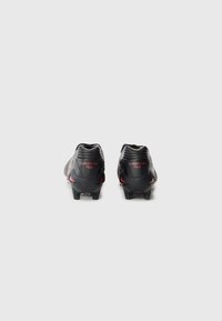 Black football cleats with red accents, textured synthetic upper, and molded rubber outsole. Heel features "MONARCIDA NEO" branding.