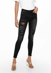 Jeans skinny negros con dobladillos deshilachados, que presentan múltiples cortes desgastados. Combinados con sandalias transparentes de tacón alto.