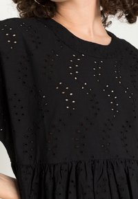 Vestido de algodón negro con patrones de flores recortados y un cuerpo texturizado, con una cintura fruncida y mangas cortas.