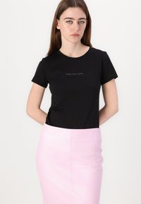 Svart bomull t-skjorte med korte ermer, med en liten logo i mørkegrå. Kombinert med en tettsittende, lys rosa pencil skirt.