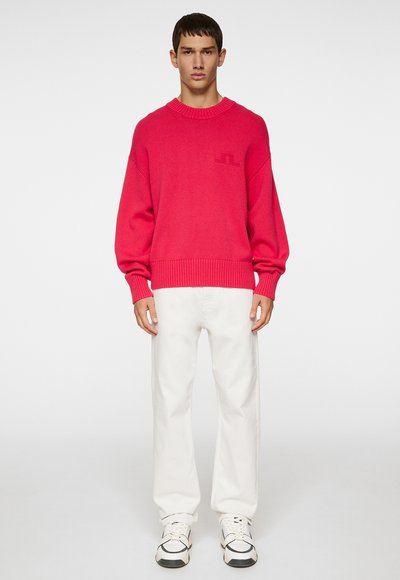 Fuchsia oversized trøje med rund hals og ribbet kant, paired med hvide straight-leg bukser og hvide sneakers med sorte detaljer.