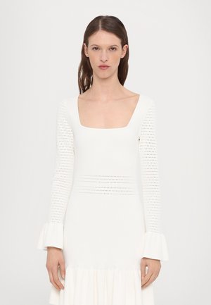 White knitted dress with a square neck, long sleeves featuring perforated details, and ruffled cuffs at the wrists, flowing into a flared hem.