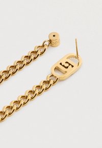 Die goldenen Kette-Ohrringe verfügen über ein geschwungenes Design mit einem Akzentstück, das ein Ausschnitt zeigt. Glatte, glänzende Textur mit einer polierten Oberfläche.