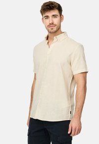 Kortekool linnen shirt in lichtbeige met een knoopkraag, met een rechte snit en subtiele textuur. Klein merkembleem aan de zijkant.