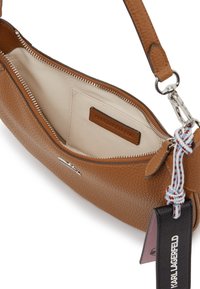 Borsa in pelle marrone texturizzata con chiusura a zip, interno beige e tracolla rimovibile. Presenta un'etichetta con logo e dettagli in pelle brandizzati.
