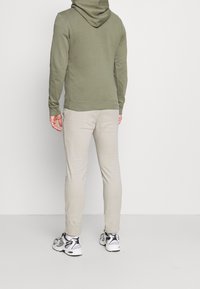 Felpa verde oliva con cappuccio foderato, abbinata a pantaloni beige chiaro. Presenta polsini e vita elasticizzati; indossata con scarpe da ginnastica grigie e nere.