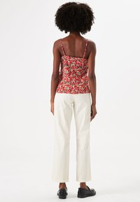 Rood cami-top met bloemenpatroon en dunne bandjes, gecombineerd met hoge witte broek en zwarte schoenen. Glad stoffen textuur.