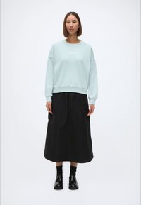 Gaiši zila sporta krekls ar "XOXO" tekstu, kombinēts ar melnu, plūstošu svārku līdz teļiem. Modelis valkā melnas zeķes un apavus. Vienkāršs dizains.